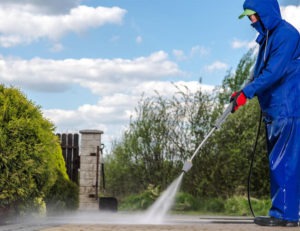 A Diamond Property Wash worker pressure washing a dirty concrete driveway outside in the sun.