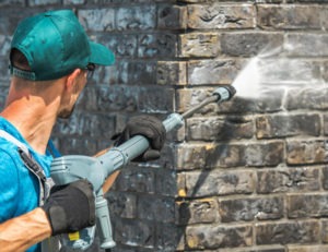 A Diamond Property Wash worker pressure washing a dirty post construction site outside in the sun.